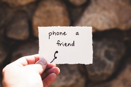 a hand holding a piece of scrap paper that reads "phone a friend"