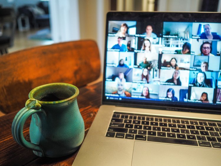 a blue mug is sitting next to a laptop that has a video call showing on the screen