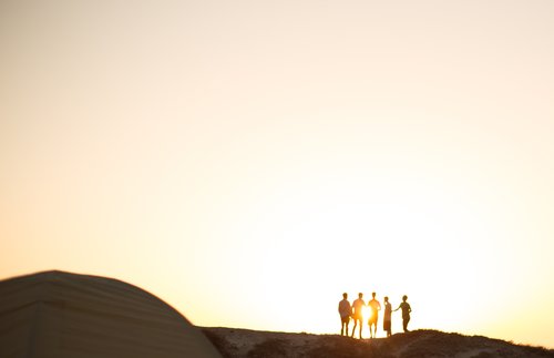 a group of people are standing far away from the camera and are backlit by the rising sun