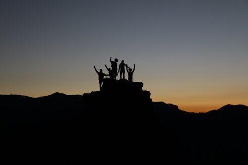 a group of people are standing on the top of a small mountain during the sunset